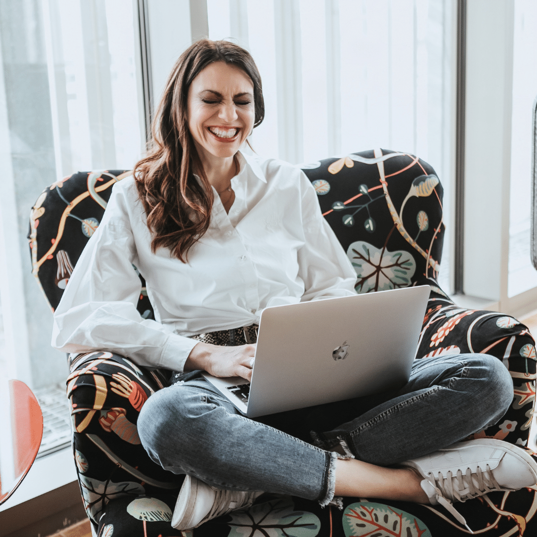 Melanie Lindner – lacht mit Laptop auf Stuhl